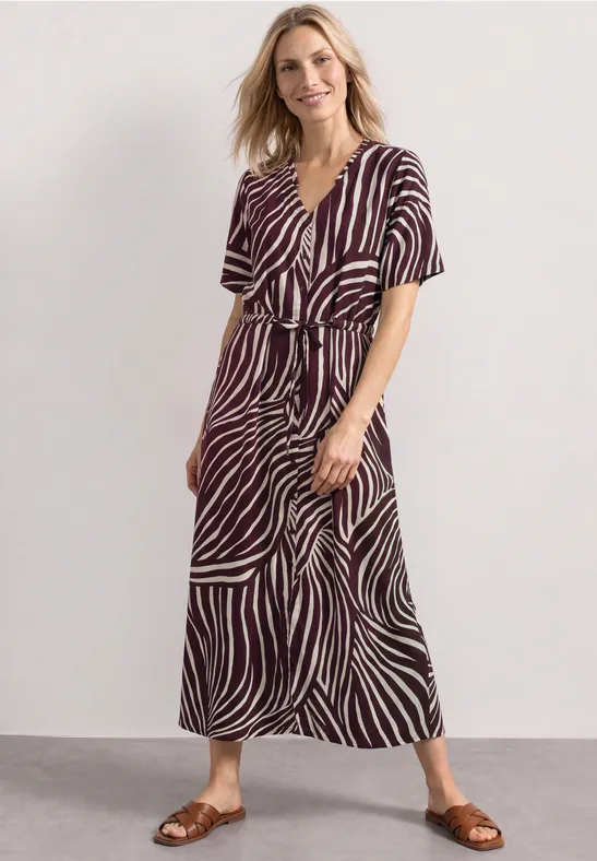 Femme en robe midi à manches courtes, motif rayé blanc et marron, col en V, portée avec sandales plates.