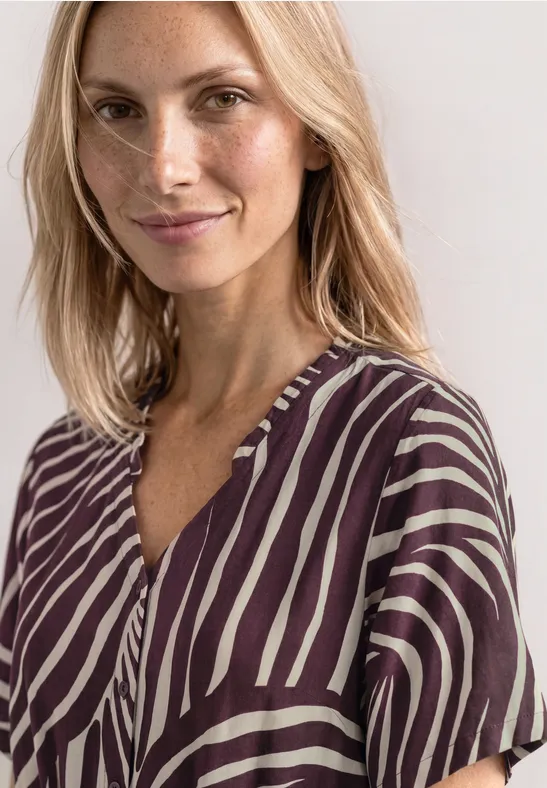 Femme aux cheveux blonds porte chemisier violet et blanc à motif zèbre et col en V.