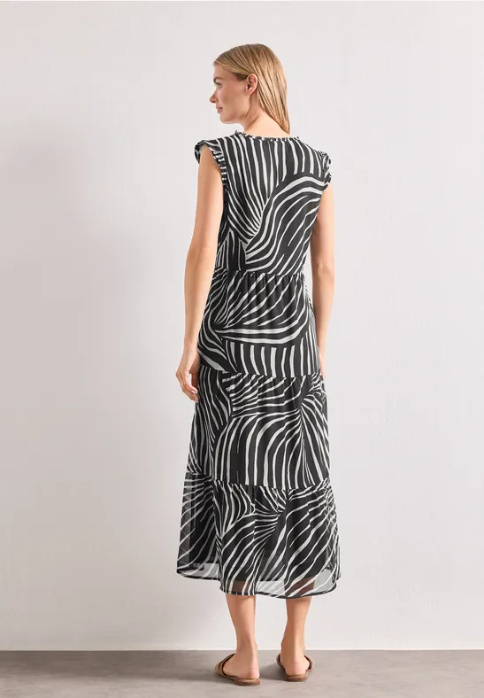 Frau im schwarz-weiß gestreiften Midikleid im Zebramuster, von hinten seitlich vor hellem Hintergrund.