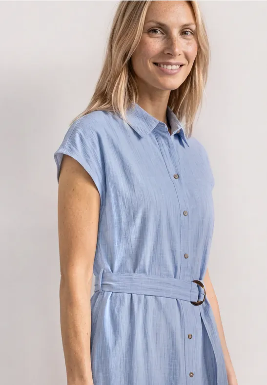 Een vrouw draagt een lichtblauw overhemdjurk met korte mouwen en ceintuur in de taille.