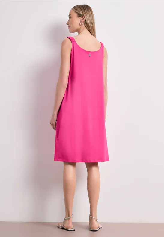 Frau in ärmellosem pinkfarbenem Kleid, Rückenansicht, mit flachen Sandalen.