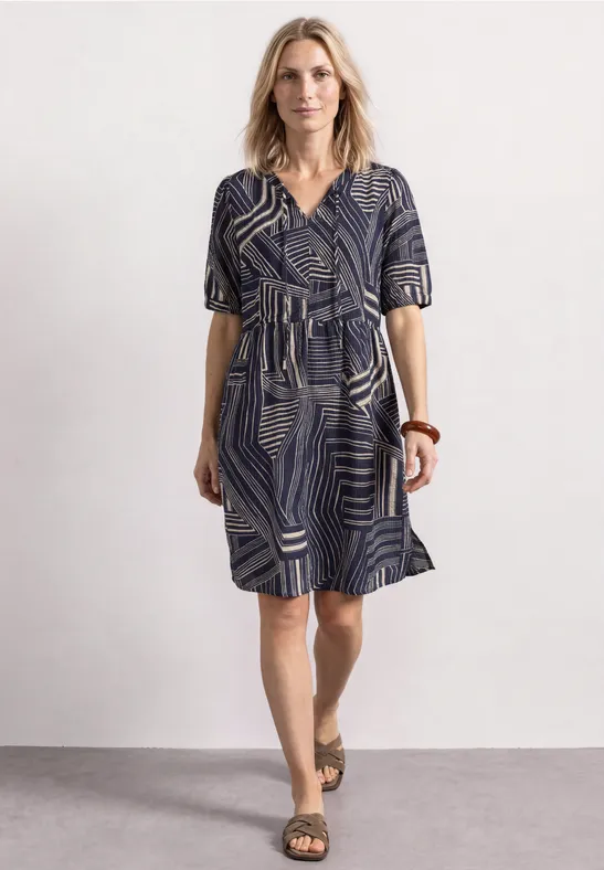 Eine Frau trägt ein blau-weiß gemustertes, knielanges Kleid mit V-Ausschnitt, kurzen Ärmeln und Sandalen.