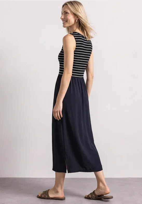 Femme de profil portant un haut sans manches rayé, un pantalon jupe large noir et des sandales marron.