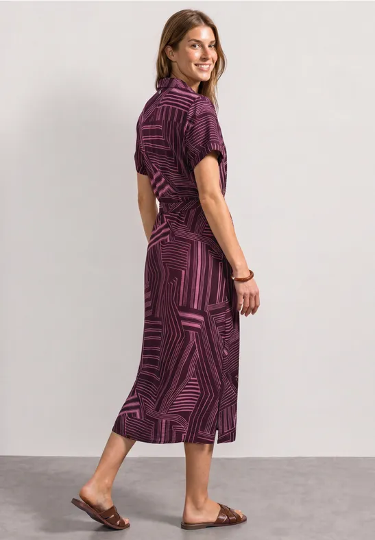 Frau in violettem, gemustertem Midikleid und flachen Sandalen.