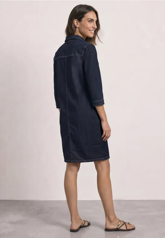 Frau in knieumspielendem Jeans-Hemdkleid mit 3/4-Ärmeln und flachen Sandalen.