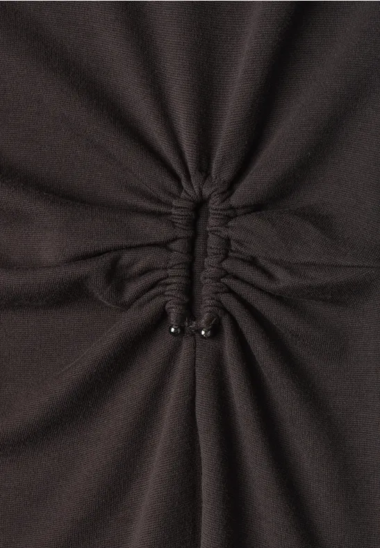 Gros plan sur un tissu sombre froncé au centre, resserré par un cordon terminé par deux embouts métalliques.