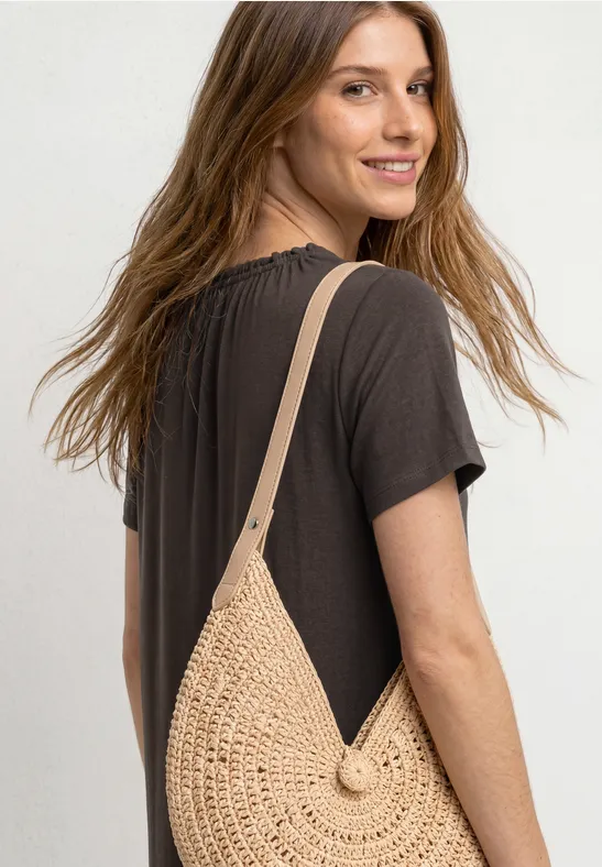 Vrouw van achteren in zwarte jurk met ronde, beige stro schoudertas.