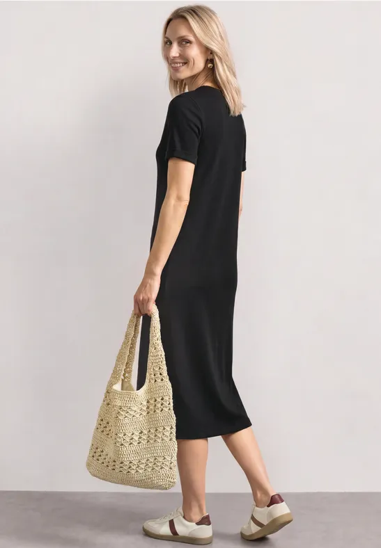 Frau im schwarzen Midikleid mit gehäkelter Tasche und Plateau-Sandalen.