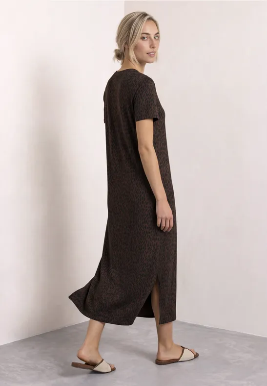 Vrouw in donkerbruine midi-jurk met korte mouwen en zijsplit, gecombineerd met sandalen, lichte achtergrond.