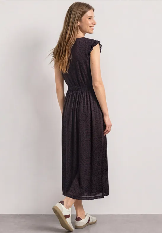Frau von hinten in schwarzem Midi-Kleid mit Volants und weißen Slip-On-Sneakern.