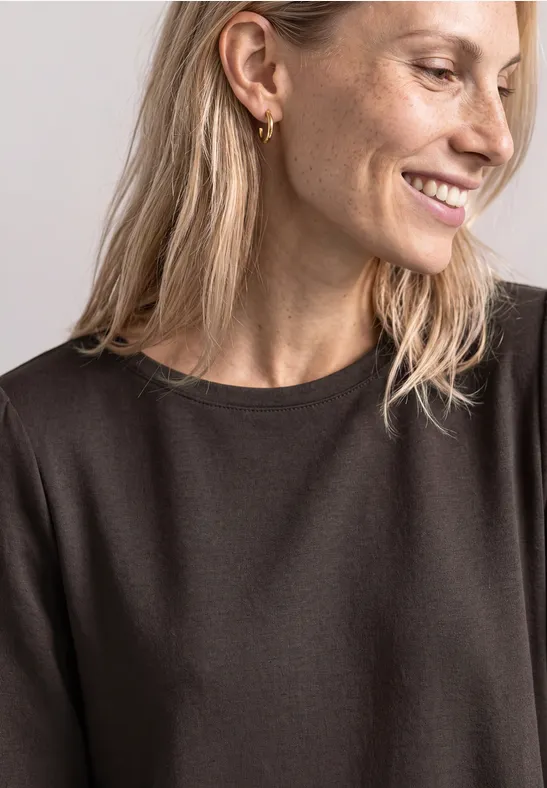 Portrait d'une femme souriante aux cheveux blonds, portant des boucles d'oreilles dorées et un haut noir.