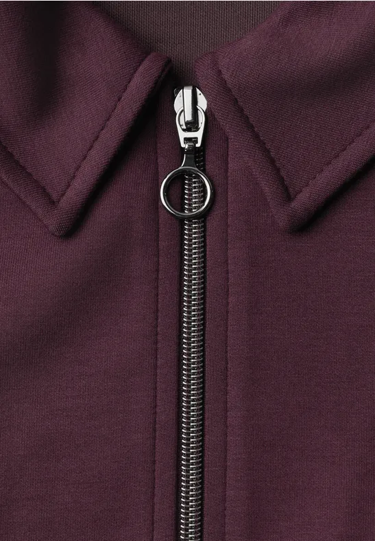 Close-up van een bordeaux kledingstuk met centrale rits en ronde ritslip.