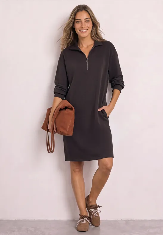 Femme en robe sweat noire à demi-zip, poches et accessoires marron, style décontracté.