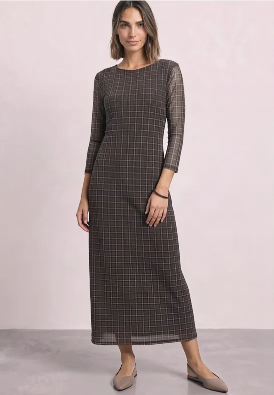 Frau in langem kariertem Maxikleid mit 3/4-Ärmeln, dezenter Farbpalette, flache Schuhe.