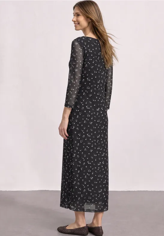 Frau in langem schwarzem Kleid mit kleinem Blumenmuster, von hinten gesehen