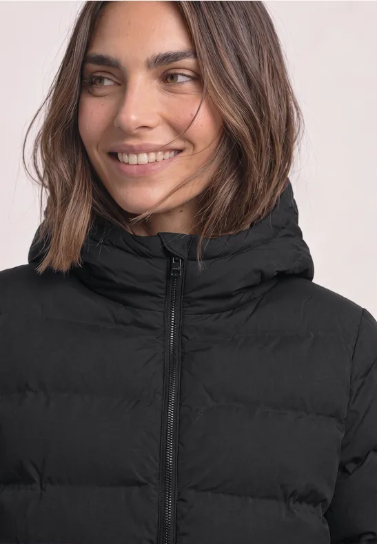 Eine lächelnde Frau trägt eine schwarze, gesteppte Winterjacke mit Kapuze.
