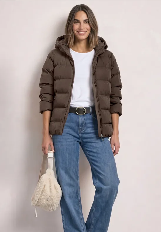 Femme portant un manteau matelassé marron, un t-shirt blanc, un jean bleu et un sac pelucheux.
