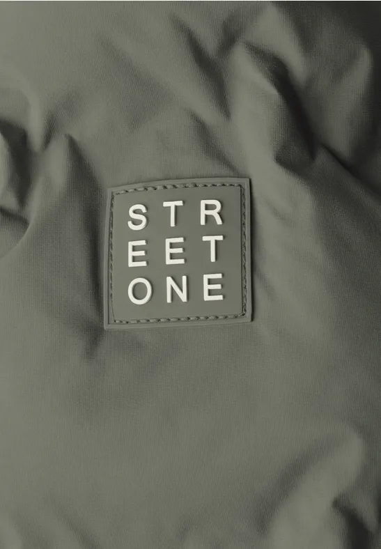 Un écusson olive avec l'inscription blanche 'STREET ONE' cousu sur une veste.