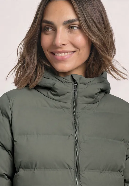 Femme souriante portant une doudoune matelassée vert olive à capuche.