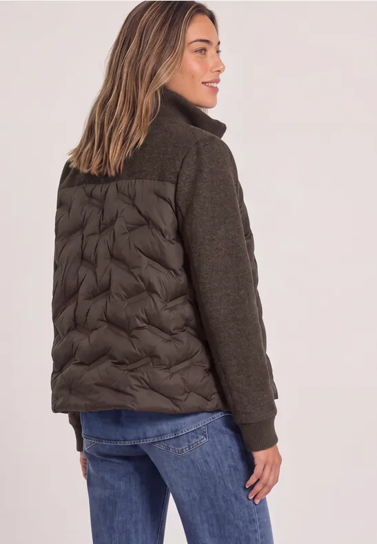 Frau von hinten in modischer Jacke mit gesteppter Rückenpartie und Strickärmeln, getragen zu Jeans.