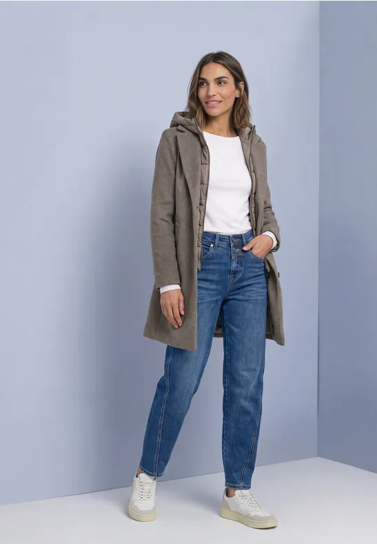 Femme en manteau kaki à capuche, top blanc, jean bleu taille haute et baskets blanches.