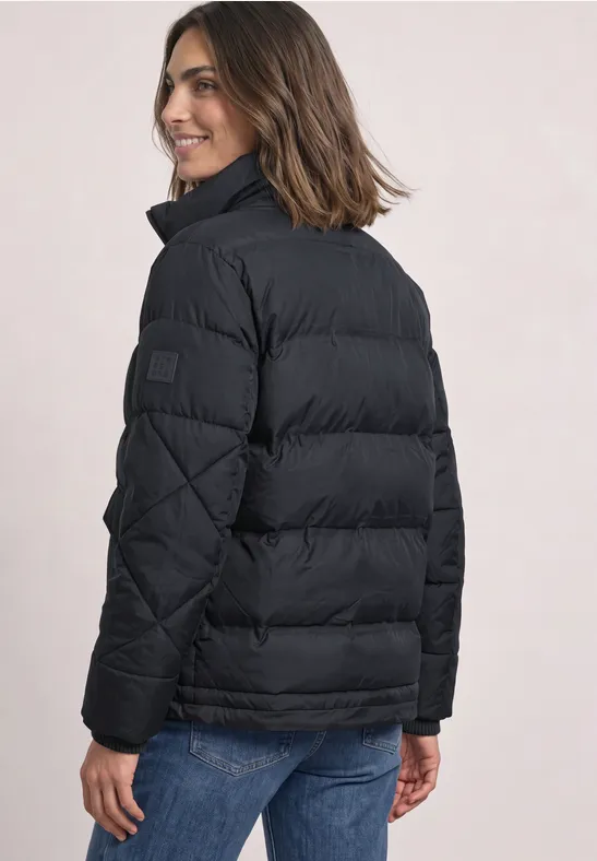 Frau von hinten in schwarzer Steppjacke und blauer Jeans, sie lächelt über die Schulter.