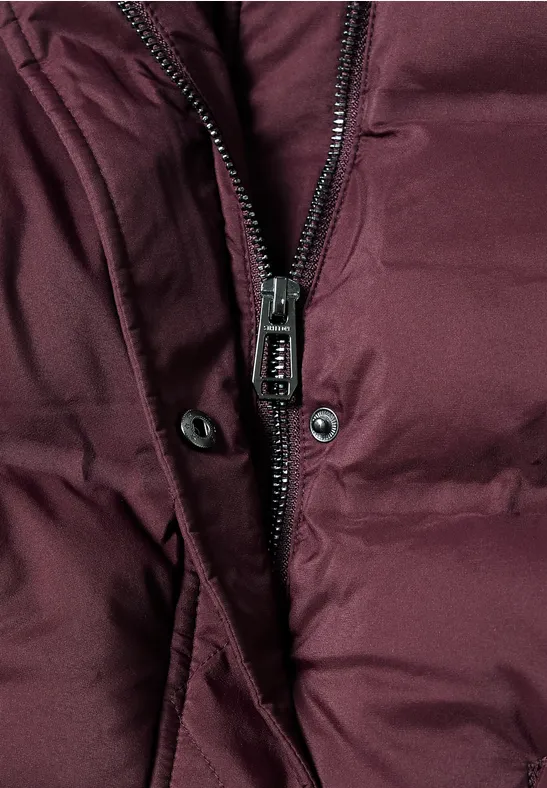 Close-up van een donkerrode gewatteerde jas met rits en drukknopen.