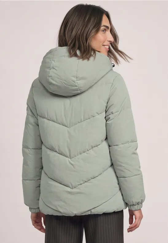 Frau von hinten in hellgrüner Steppjacke mit Kapuze.