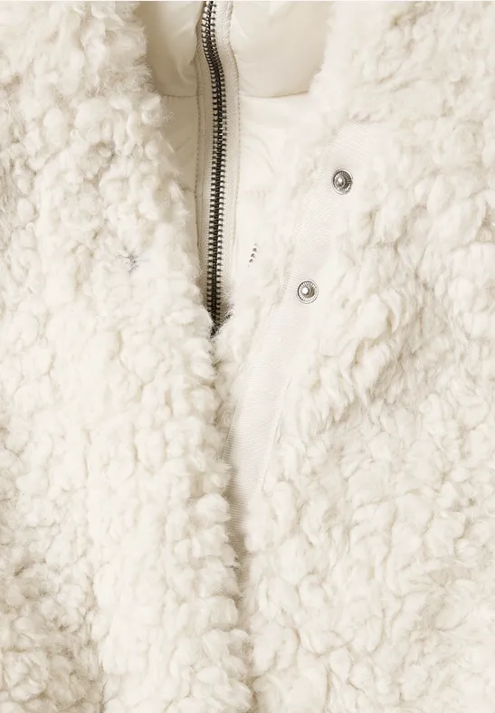 Nahaufnahme einer cremeweißen Teddy-Fleece-Jacke mit Reißverschluss und Druckknöpfen.