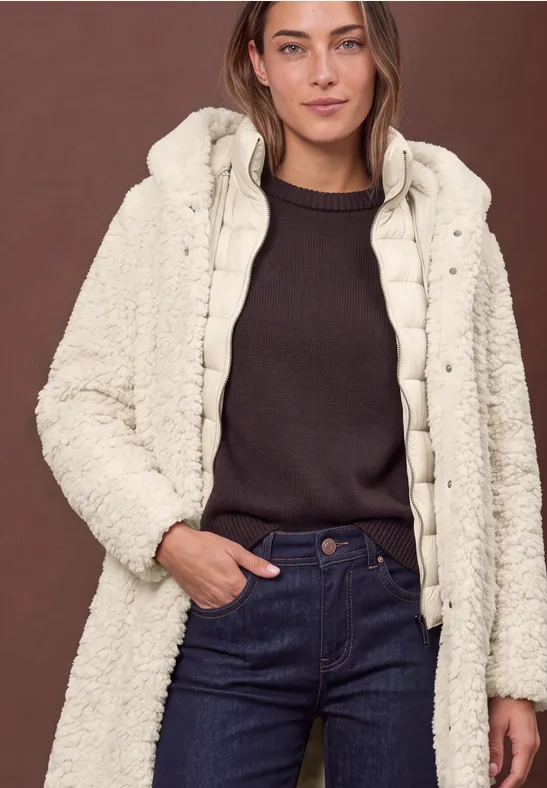 Femme en jean et pull sombre portant une veste matelassée crème à capuche en tissu duveteux