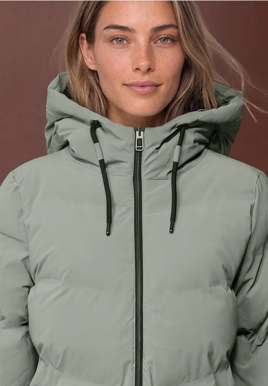 Eine Frau mit hellgrau-grüner Steppjacke mit Kapuze und Reißverschluss.