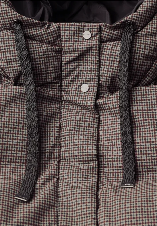 Nahaufnahme einer karierten, wattierten Jacke mit Kapuze und dicken, schwarzen Kordeln sowie silbernen Druckknöpfen.