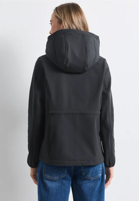 Rückansicht einer Person in schwarzer Kapuzenjacke und blonden Haaren, trägt blaue Jeans.