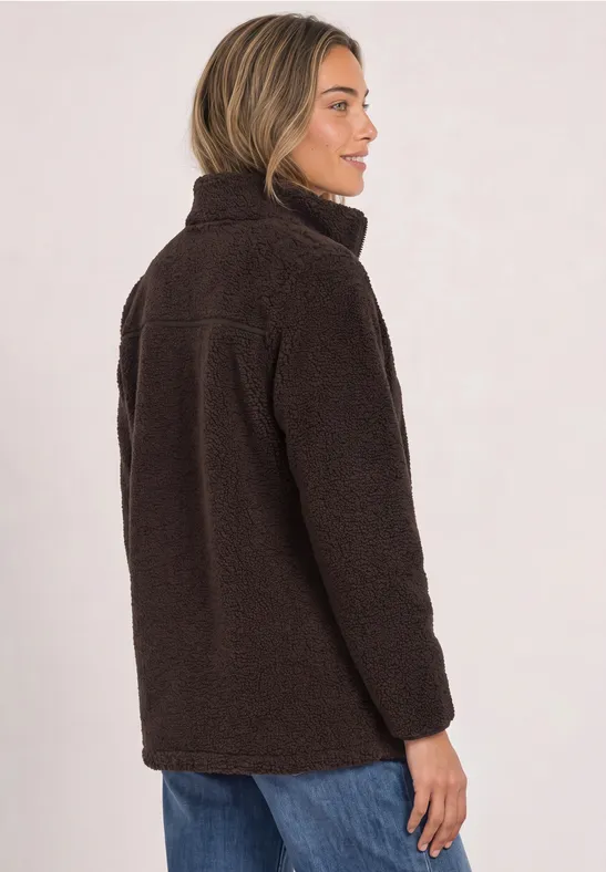 Frau in dunkelbrauner Teddy-Fleecejacke mit Stehkragen, seitlich im Profil, dazu blaue Jeans.