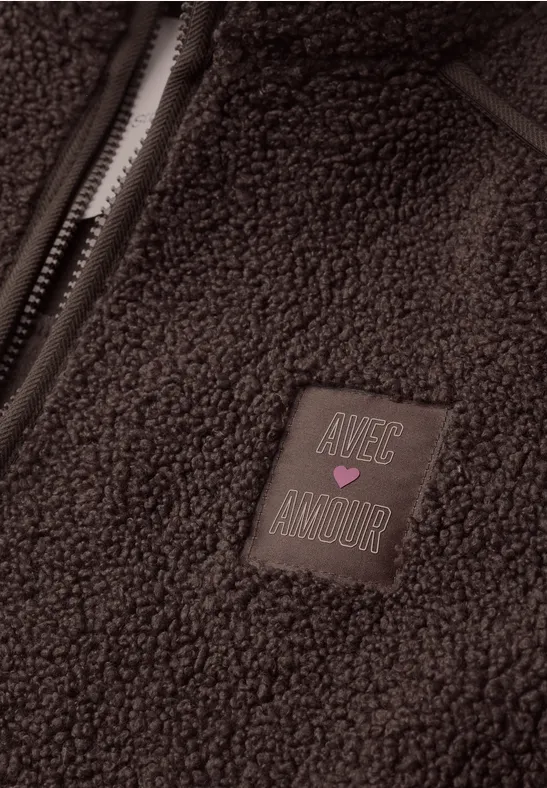 Ein brauner Teddy-Fleece mit Reißverschluss und einem Patch mit Schriftzug 'Nice Amour' und rosa Herz.
