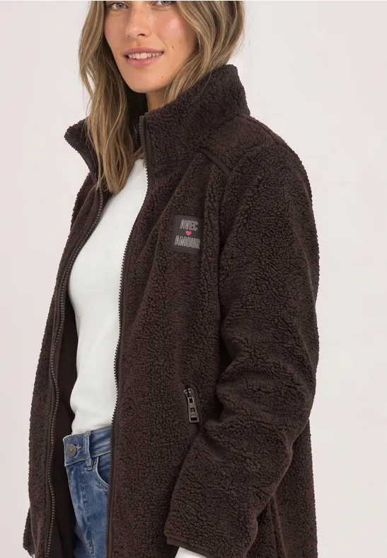 Frau in brauner Teddy-Fleecejacke mit Reißverschluss, kombiniert mit weißem Top und Jeans.