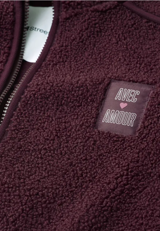 Gros plan d’une veste polaire bordeaux avec patch 'AVEC AMOUR' et fermeture éclair.