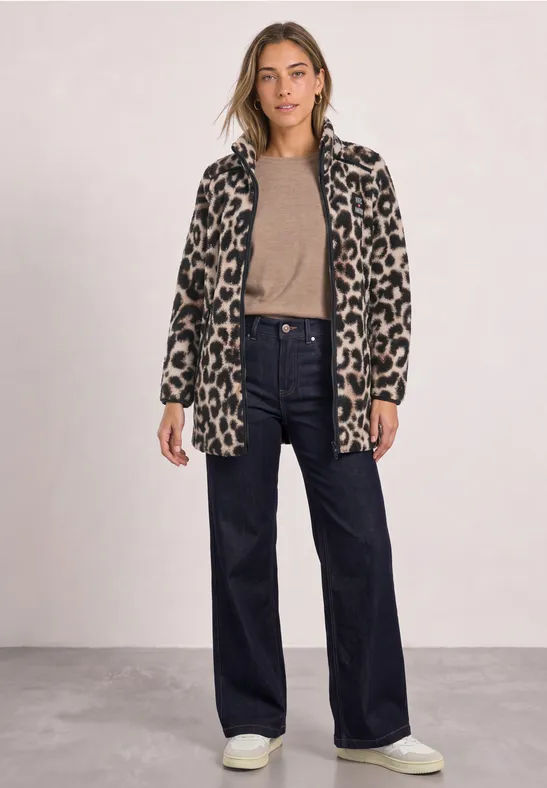 Frau trägt Leoparden-Mantel, beigefarbenen Pullover, weite Jeans und weiße Sneaker.