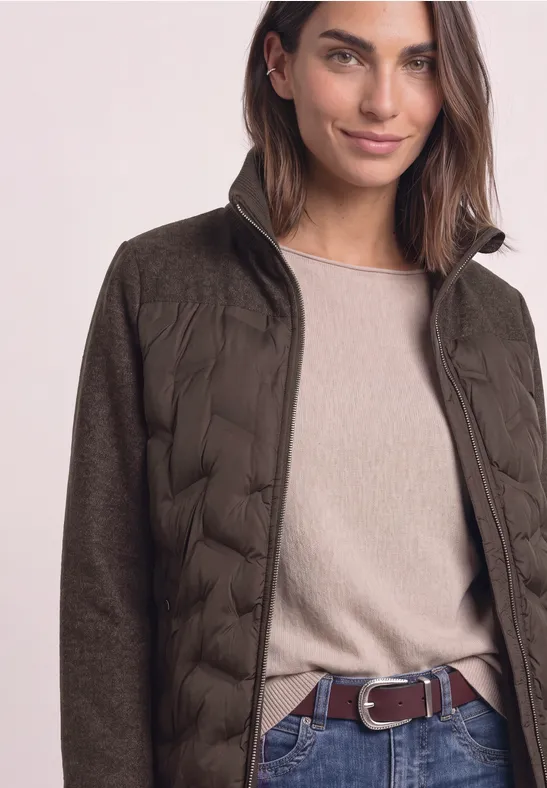 Frau in olivgrüner Steppjacke mit beigem Pullover und braunem Gürtel.