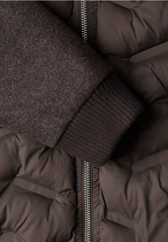 Nahaufnahme eines dunkelgrauen Steppmantels mit Reißverschluss und einem Strickbündchen