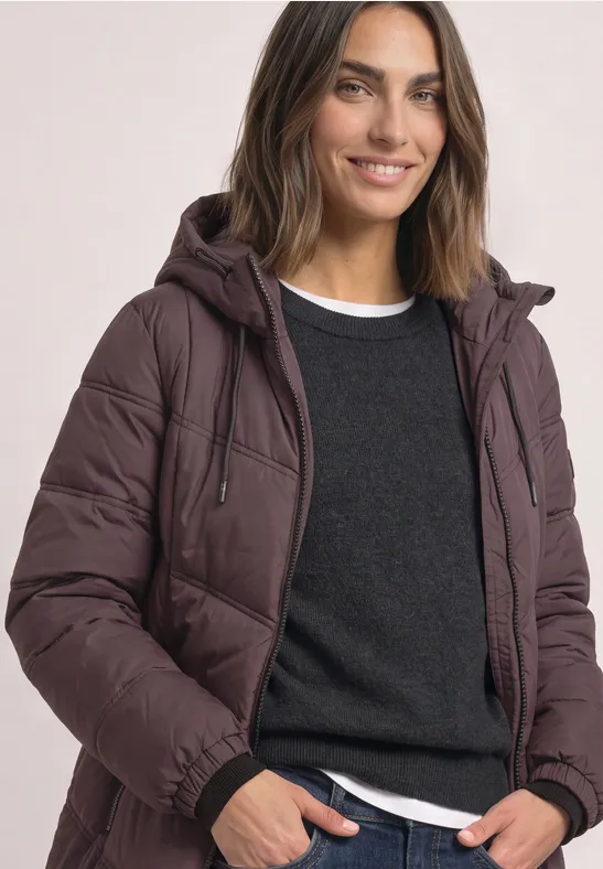Frau in einer gefütterten Kapuzenjacke, mit Pullover und T-Shirt, lächelt in die Kamera.
