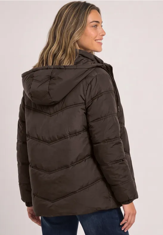 Eine lächelnde junge Frau von hinten mit dunkler, gesteppter Winterjacke und Kapuze.