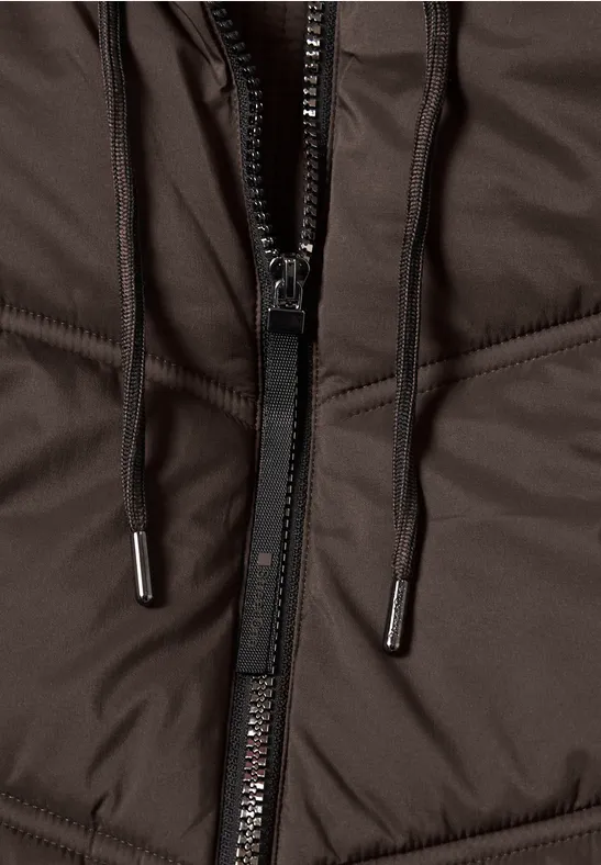 Nahaufnahme einer braunen wattierten Jacke mit Reißverschluss und schwarzen Kordeln mit Metallenden.