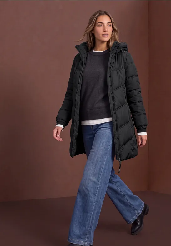 Frau trägt schwarzen, wattierten Wintermantel und Jeans und geht selbstbewusst.
