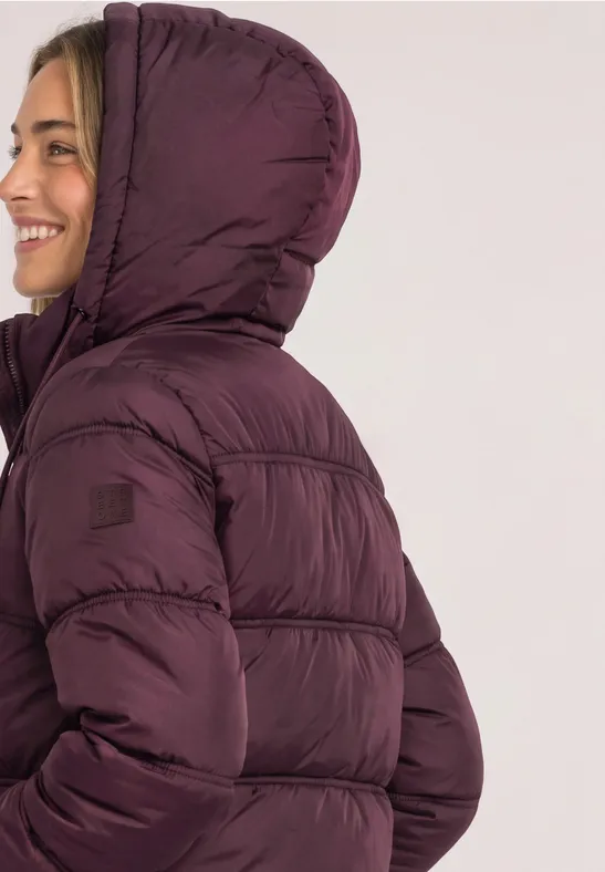 Frau im Profil mit einer lila Steppjacke mit Kapuze, die lächelnd nach links blickt.