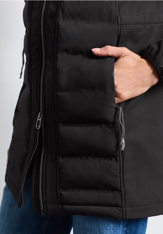 Veste matelassée noire avec fermeture éclair, main dans la poche latérale.