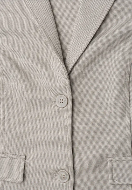 Close-up van een beige blazer met knopen en zakken.