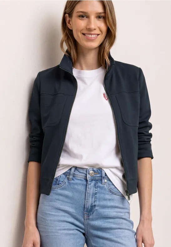 Eine Person trägt ein weißes T-Shirt, blaue Jeans und eine dunkelblaue Jacke.