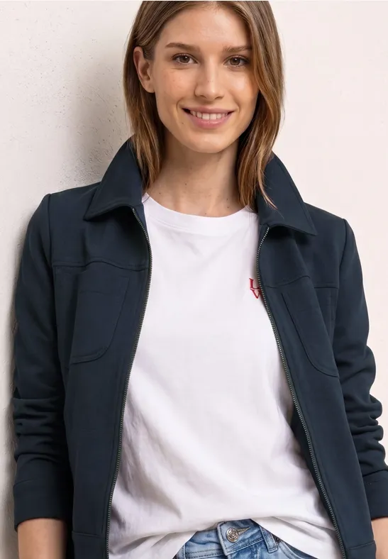 Person trägt dunkelblaue Jacke über weißem T-Shirt vor hellem Hintergrund.