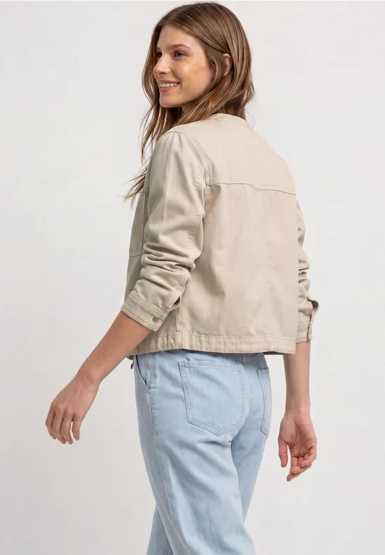 Persoon van achteren, draagt een beige jas en lichtblauwe spijkerbroek tegen witte achtergrond.